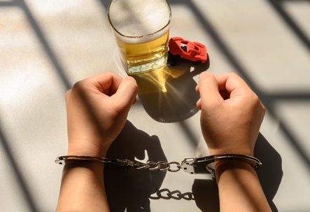 Person in handcuffs next to glass of alcohol