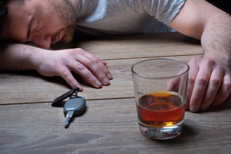 Man asleep next to keys and glass of alcohol